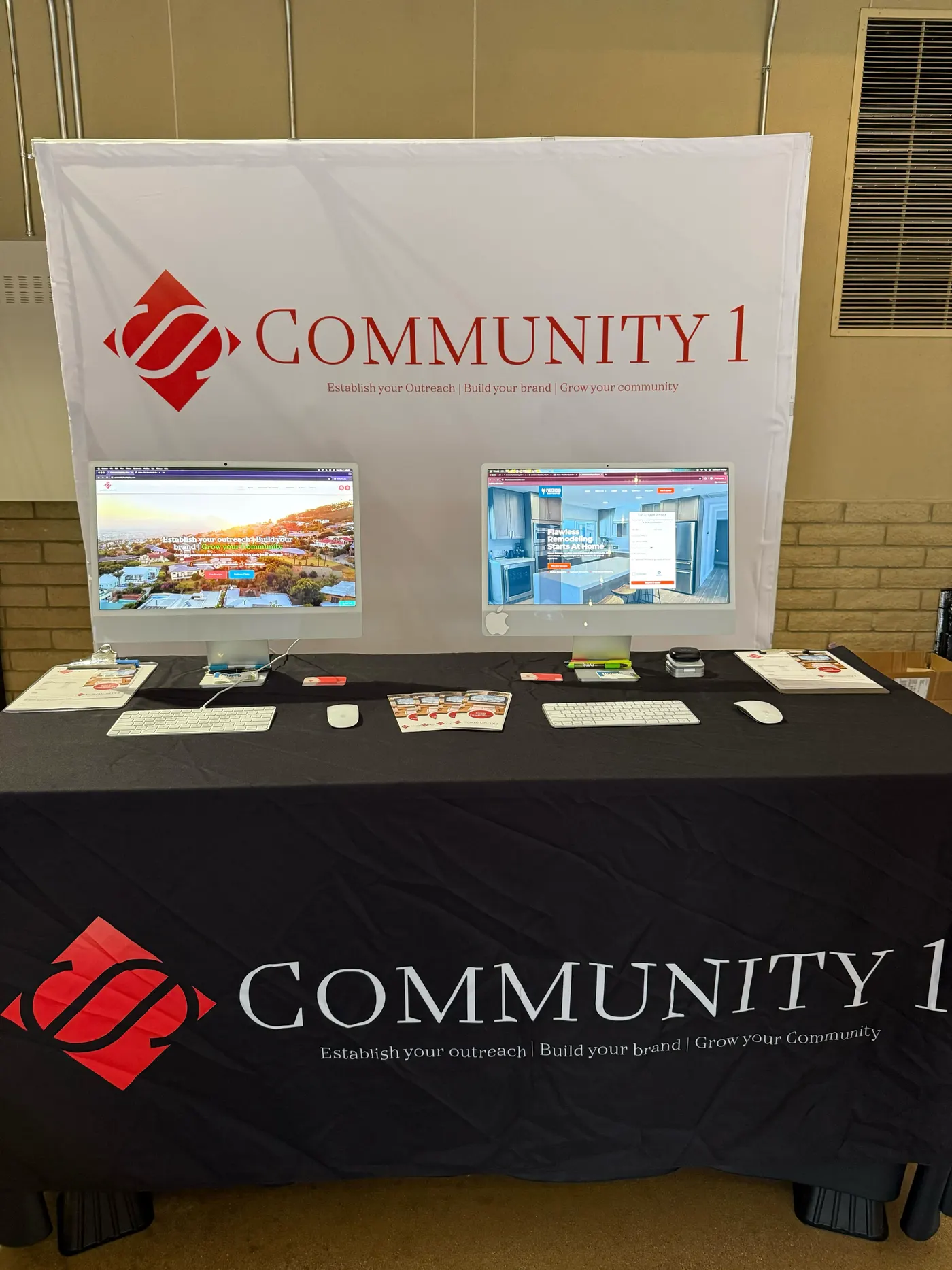 The Community 1 booth with its red diamond banner and two monitors showing client websites